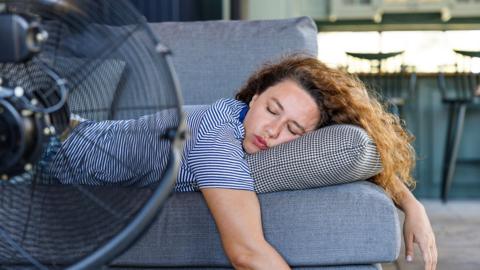 A woman sleeping in front of a fan on the sofa