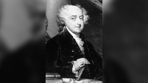 A black and white portrait of John Adams. He is looking to the right hand side of the portrait, wearing a dark jacket and white frilled neckerchief. He has a bald top of the head with white curly hair around the edge of his head. He is resting his hand on a book. 