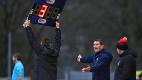 Mansfield boss Nigel Clough talking to a fourth official as he hold up a board to indicate how many additional minutes are to be played