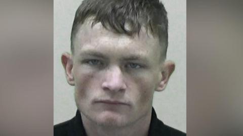 Mugshot of Shaun Hodgson. He has a menacing expression and is clean shaven with short dark hair.