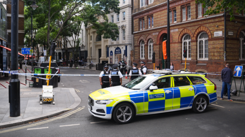 Police officers stand around a cordon with a police vehicle Endell Street in Covent Garden, central London