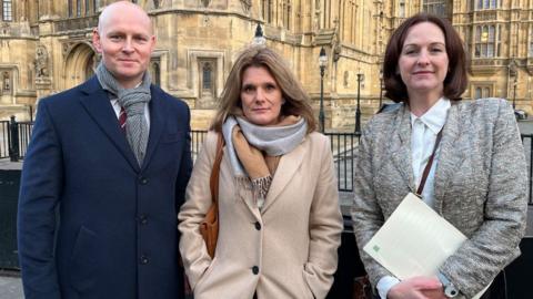 General view, Ellen Roome Max Wilkinson Lola Mcevoy outside parliament for jools law debate. They are wearing winter coats and looking at the camera with the Houses of Parliament in the background