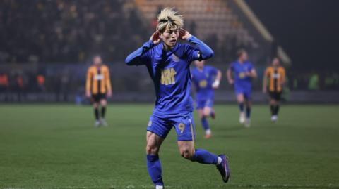 An image of Kyogo Furuhashi, wearing his blue Birmingham City home kit, celebrating his goal in January by holding his hands to his ears
