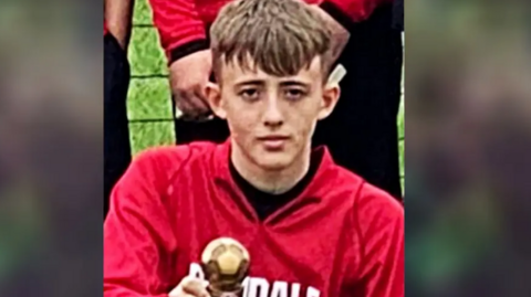 Harry Parker holding a trophy, looking at the camera. He has short brown hair and is wearing a red top.