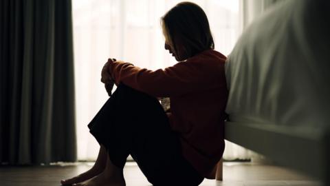 In silhouette of woman sitting on a bedroom