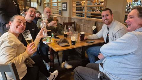 A pub table full of people celebrating with a pint