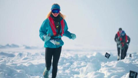 A woman in a bright blue coat and black leggings runs through the snow