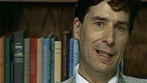 John Cairncross sits in front of a shelf of books.