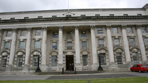 Belfast Crown Court, a stone building with two black lampposts at the front door. There are white-framed windows and tall, stone columns across the front.