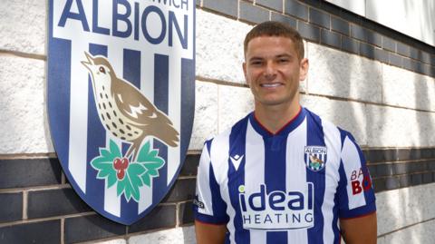 Conor Townsend poses in a blue and white striped West Bromwich Albion kit