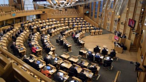 A general view of the Scottish Parliament chamber, with MSPs sitting at wooden desks in a semi-circle facing the speak, who is on a raise wooden platform 