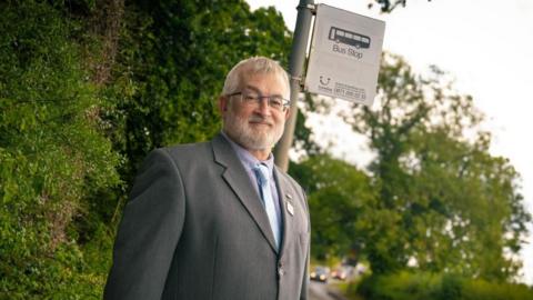 A man in a suit stands by a bus stop