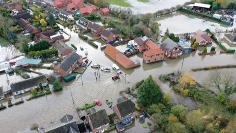 An aerial view of the village of Fishlake when it was flooded in 2019, showing houses and trees surrounded by water and cars afloat nearby 