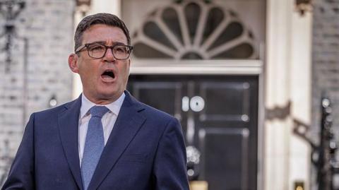 Andy Burnham in a navy suit and light blue tie speaks outside the black front door of 10 Downing Street in central London.