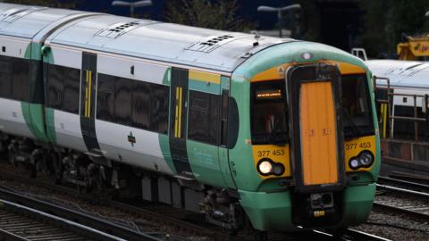 The front of a Southern train which is green and yellow and is moving along a track. A track can be seen either side of the train and the train has one light on its front