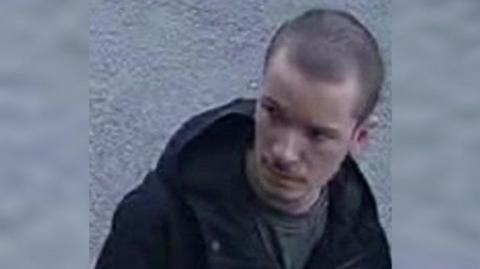 CCTV image of Sam. He has short dark hair and is wearing a dark jacket 