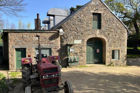 A picture of the Sark Electricity power station with a red tractor outside. The building is brickwork with green doors and panels.