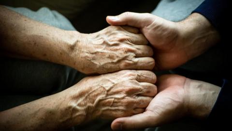 A pair of hands, with what appear to be an older person's hands in another's person's hands