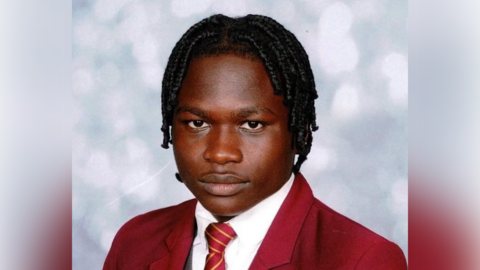 A school photo of Iretomiwa Abiodun Micheal, who has braided, black hair, and is wearing a red blazer, a white shirt, and a red and yellow striped tie.