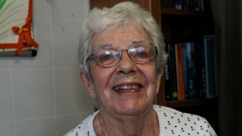A head and shoulders image of a woman wearing glasses and a white top. She is looking into the camera while smiling. 