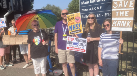 Members of NHS staff hold placards at a protest.