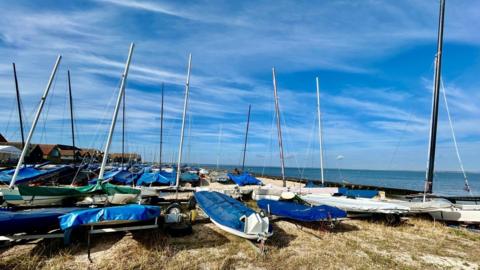 Several small sail boats on the sand with sea and blue sky behind