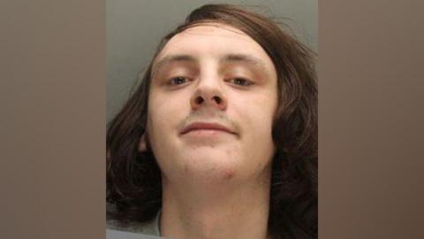 Police image of James Foy, who has long brown hair and a grey sweatshirt on