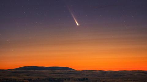 A long-exposure photo of a comet streaking across a night sky.