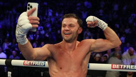 Josh Padley flexing his bicep while taking a selfie in the ring