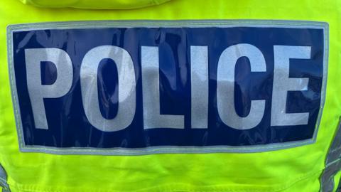 Close up of the words police in white letters on a blue background on the back of a yellow high-visibility jacket