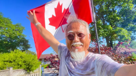 Dong Guangping posing in front of a Canadian flat, with his right hand holding the flag