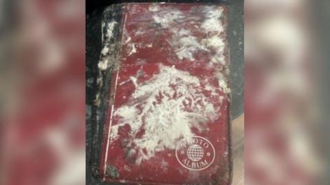 A red photo album is in the middle of the picture, with a logo on the bottom left that says 'photo album'. Lost of dust and fire damage is on the front of the album. 