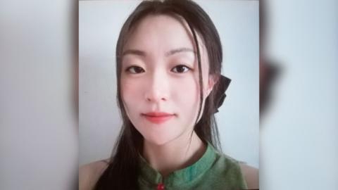 picture of Zhe Wang wearing a green top. Her dark straight hair is tied back in a pony tail and she is look straight at the camera. 