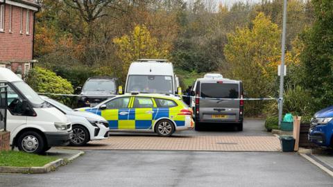 A police car is parked by a residential address in Emersons Green near Bristol. There is police tape across the car park.