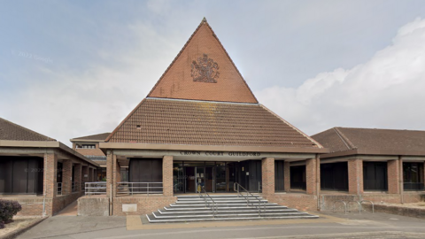 The outside of Guildford Crown Court, showing the steps leading into the building, the steepled roof of red brick and brown tiles.