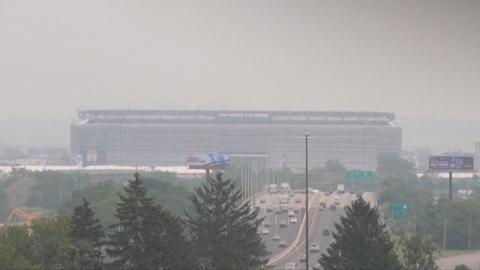 Smoke from Canadian wildfires shrouds MetLife Stadium, host of the 2026 FIFA World Cup final, as hazy orange skies reduce visibility over a busy highway in New Jersey.