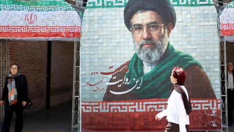 Iranians walk next to a picture of Iran supreme leader Ayatollah Mojtaba Khamenei in a street in Tehran, Iran, 06 May 2026. US President Donald Trump announced pausing the operation of escorting ships through the Strait of Hormuz, hinting at progress in peace talks with Tehran.