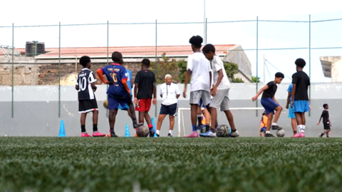 Children play football on an artificial pitch in Cape Verde while a coach oversees their progress