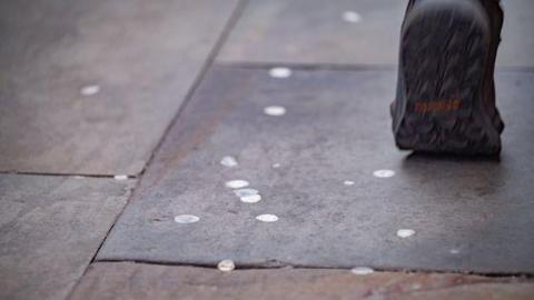 Someones foot in a shoe walking on a pavement covered in chewing gum waste