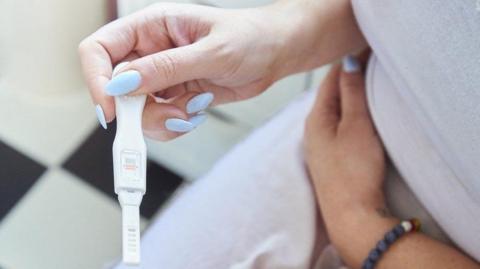 Woman holding a positive pregnancy test sat in bathroom