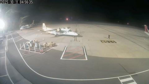 A dark image with an Aurigny plane in the foreground and a man matching Russell Payne's description walking towards the camera. 