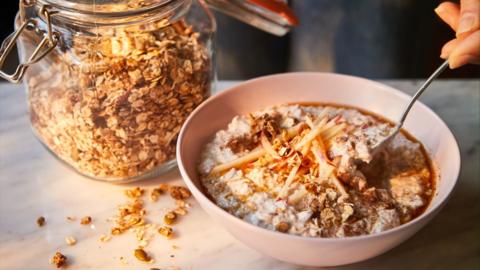 A glass jar of oats sits next to a pink bowl of oats with a spoon in it