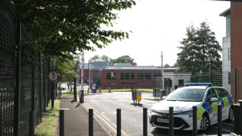 A police car is behind black bollards close to the car park where the 19-year was killed.
