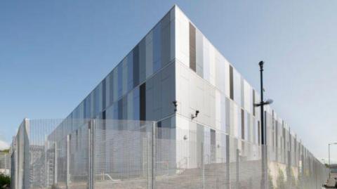A large silver data centre building, with a mesh fence surrounding it.
