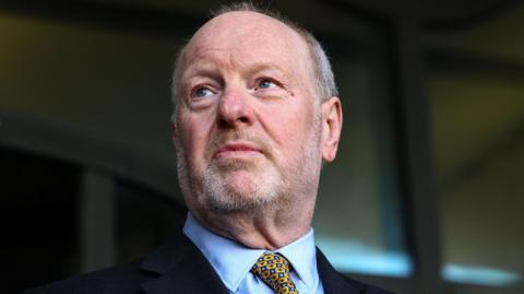A close up of a man in a suit, light blue shirt and yellow tie