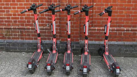 Red electric scooters parked in a line on the pavement in Bristol, England