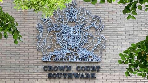 A royal crest of metal lattice on the front of a brick municipal building. Underneath black letters spell out Crown Court Southwark.