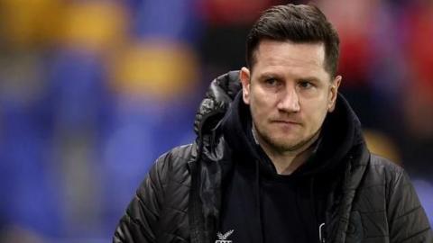 Lee Bell walks along the touchline after a game in his black Crewe puffer jacket