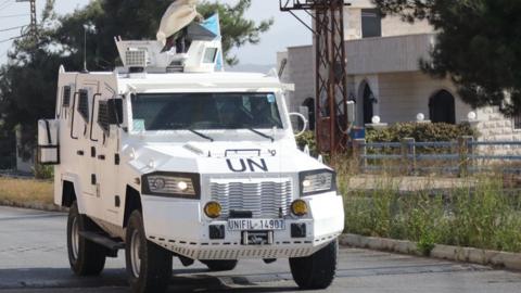 A UN vehicle - a white truck - drives on a road next to a tower