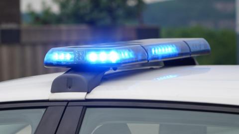 A flashing blue set of lights on top of a car which has a white roof and we can see the top of its windows.